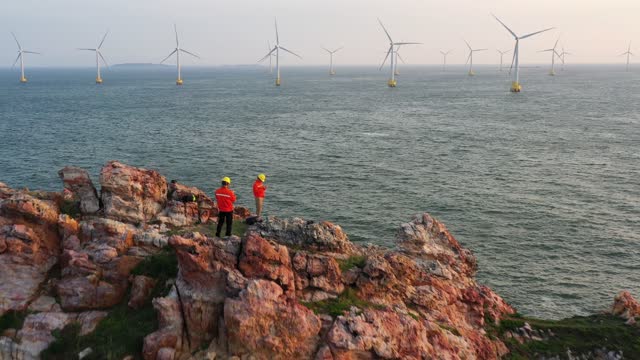 Two workers are using a drone to inspect wind turbines on the shore