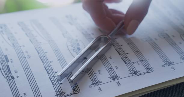 istock One woman's hand holds a tuning fork, the other traces the sheet music. 1490252920