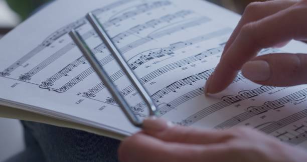 istock One woman's hand holds a tuning fork, the other traces the sheet music. 1490252925