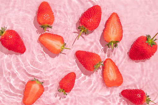 Spring summer creative layout with strawberries in pastel pink water ripple background. 80s or 90s retro aesthetic idea. Minimal summer fruit idea.