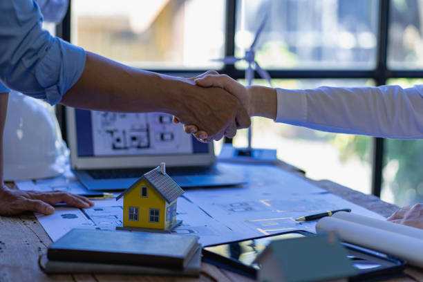 dos ingenieros o arquitectos exitosos que tienen un acuerdo manos tomadas de la mano mientras están sentados en el escritorio con paneles solares y turbinas eólicas para la electricidad del hogar. - alternative energy electricity wind turbine team fotografías e imágenes de stock