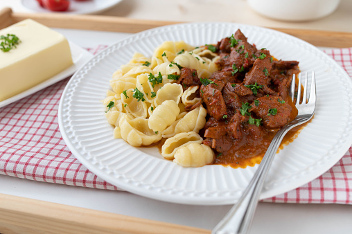Delicious homemade meat dish with pasta for sunday dinner or lunch with  strips of chicken breast in a delicious paprika cream sauce. Served with buttered shell pasta on a white plate on rustic and light background