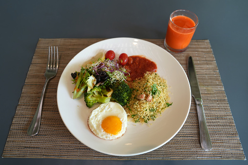 A plate of green salad consists of alfalfa sprouts, leafy vegetables, millet, baked beans, sunny side up, and a cup of carrot juice. This dish represents a healthy and nutritious eating lifestyle. High angle view.