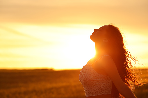 Female silhouette breathing fresh air at sunset in a field