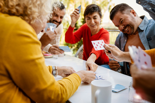 Close up on Diverse People playing cards and having fun, laughing together around the table on a house porch