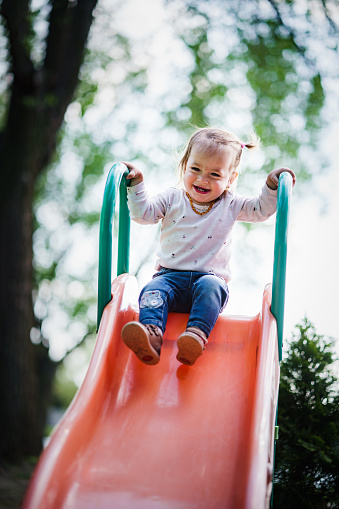 Happy little girl sliding at playground during sunny day