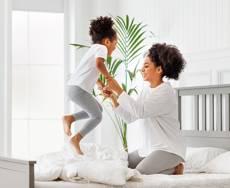 Happy ethnic family. African american kid jumping, play and laugh on bed with mother an home