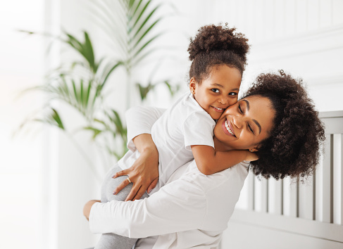 Happy ethnic family. African american mother and daughter play and laugh in bed an home