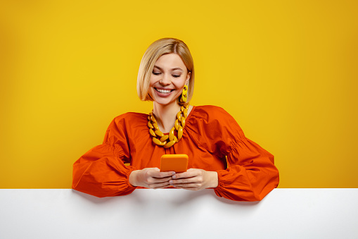 Fashionable young woman using smart phone against yellow background