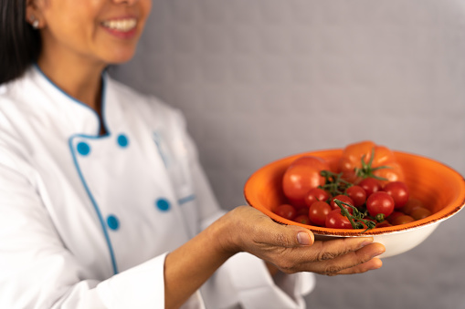 Smiling unknown female chef shows lovely bowl with fresh just picked tomatoes