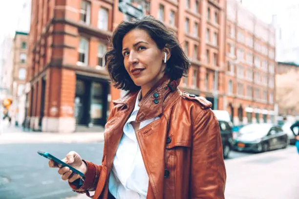 Photo of Fashionable woman walking to the office listening voice messages on earphones