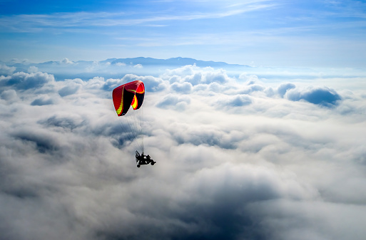 A paraglider soars gracefully over the clouds, embracing the exhilarating sense of freedom and the thrilling challenge that comes with it.