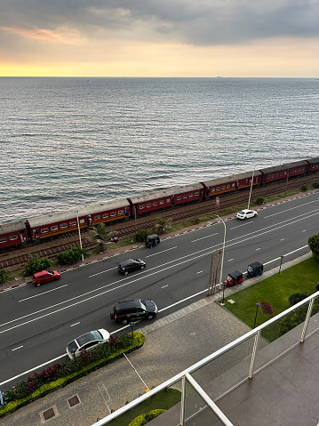 Stock photo showing elevated view of metal railway the line and gravel of southern line diesel railroad track in Colombo, Sri Lanka running parallel to the coast with waves breaking on the rocky shore.