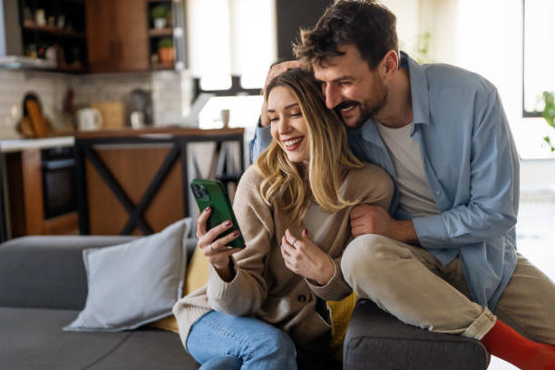 istock Smiling couple embracing while looking at smartphone. People sharing social media on smart phone. 1490280588