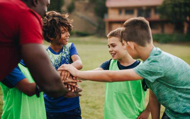 school kids having a huddle with their coach in a sports field - soccer child coach childhood imagens e fotografias de stock