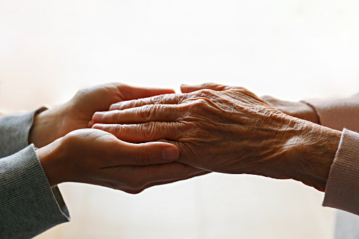 Cropped studio shot of elderly woman and female geriatric social worker holding hands. Women of different age comforting each other. Close up, background, copy space.