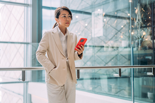 A beautiful Asian businesswoman using smartphone against modern office building in the city. e-Commerce concept.