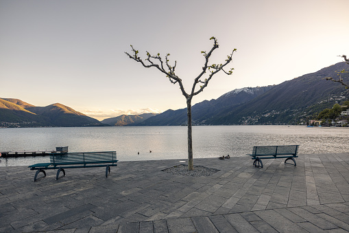 Morning view of Lake Bohinj with senior woman sitting on pier and enjoying  mountain reflection in lake water. It is in Julian Alps, Slovenia and is destination is occupied by Slovenia tourists because the coronavirus travel restrictions.  It is starting point to many hiking tours.