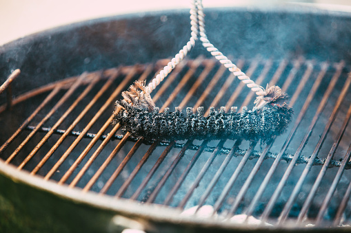 Close up of a man cleaning his barbecue grill using a brush.