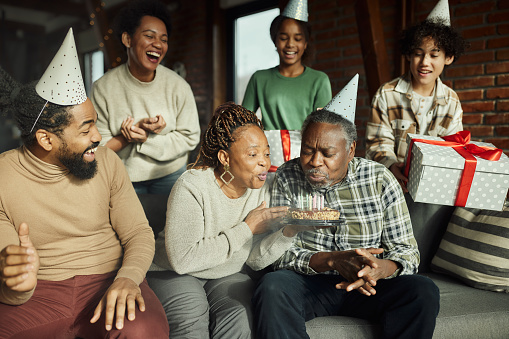 Cheerful African American multi-generation family having fun during a Birthday party at home while senior couple is blowing candles.