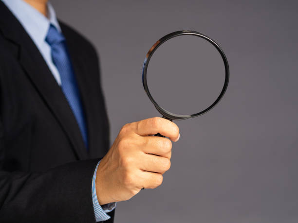 istock A businessman in a suit holding a magnifying glass while standing over a gray background 1490292586