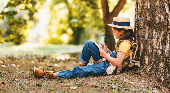 child girl traveler takes notes in a notebook while walking through the forest