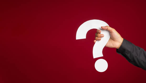 istock Hand of a man in a black shirt holding a white question mark while standing with a red background 1490292859