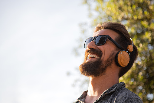 Smiling man relaxing listening to music with headphones surrounded by nature. Copy space. Wellness concept.