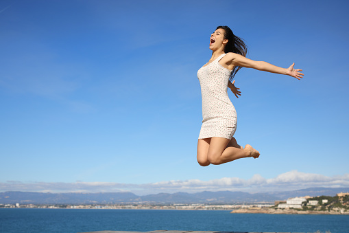 Happy woman jumping in the coast celebrating