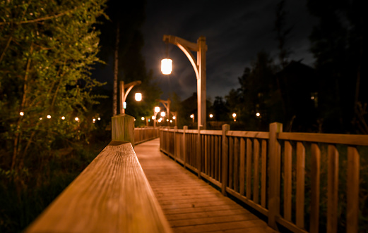 Shallow depth of field, wooden boardwalk at night with lamps through a wood