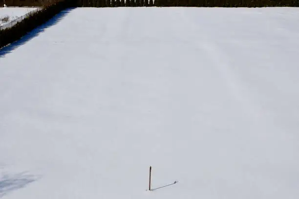 Photo of A close up on a small fire hydrant or brown metal pipe standing in the middle of a vast field covered fully with fresh snow and ice spotted on a Polish countryside on a sunny winter day