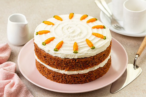 Table with homemade carrot cake made with carrots, walnuts, iced with cream cheese. Chocolate decoration. Sweet dessert. Beige background.