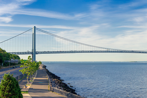 Verrazano-Narrows Bridge on a summer morning with Promenade and Cars driving on the Belt Parkway. The bridge connects boroughs of Brooklyn and Staten Island in New York City. The bridge was built in 1964 and is the largest suspension bridge in the USA. The photo was taken from the Shore promenade in Bay Ridge Brooklyn. Canon EOS 6D full frame censor camera. Canon EF 85mm F/1.8 lens. 3:2 Image Aspect Ratio.
