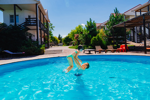 Dad and daughter play in the pool. Joyful moment captured as dad throws daughter in the air. Perfect for family vacation and summer activities themes.