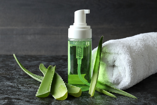 Aloe leaves, cosmetic and towel on black smokey table