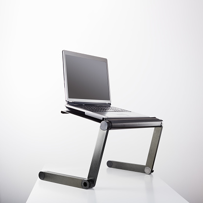 Laptop computer sits on a portable holder riser or stand against white background