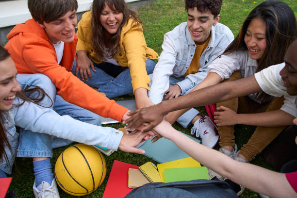 istock Multiracial group of cheerful young students joining hands in circle sitting on grass outside campus 1490306855