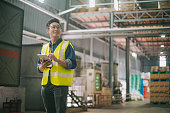 Satisfied Asian Chinese warehouse worker taking inventory looking away with digital tablet in logistic warehouse