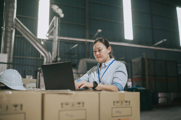 Asian Chinese female factory warehouse foreperson using laptop planning logistic shipment stock photo