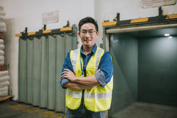 asiatischer chinesischer männlicher lagerarbeiter arme verschränkt mit blick auf kamera lächelnd - manager foreman warehouse arms crossed stock-fotos und bilder