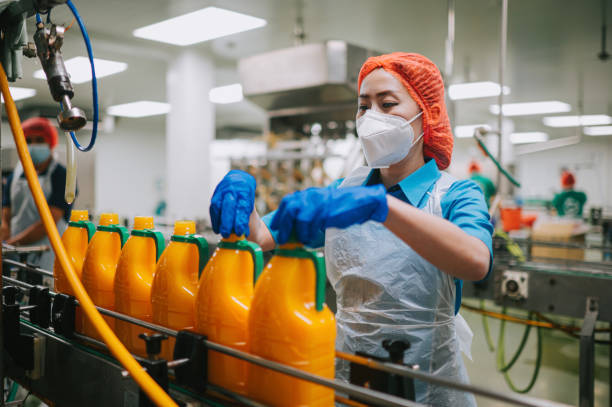 asiatische chinesische saftfabrikarbeiterin zieht flaschenverschluss in produktionslinie fest - industriearbeiter stock-fotos und bilder