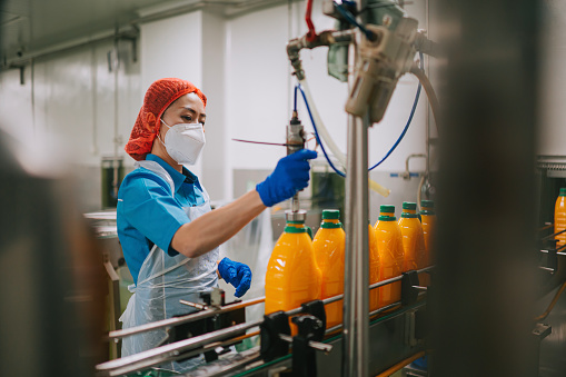 Asian Chinese female juice factory worker filling up orange juice in production line