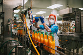 Asian Chinese female juice factory worker cleaning juice bottle with water hose in production line