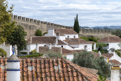 Obidos, Portugal-September 2022; Panoramic view over the orange tiles roofs with typical medieval architecture and the walls of the Castle of Obidos in the background