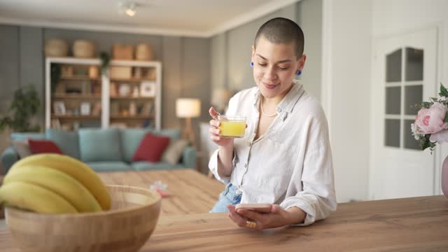 A young beautiful woman is drinking juice from a squeezed orange during the morning while in her kitchen