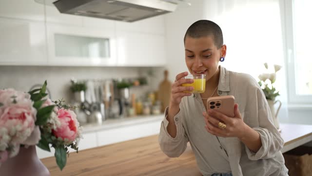 A young beautiful woman is drinking juice from a squeezed orange during the morning while in her kitchen