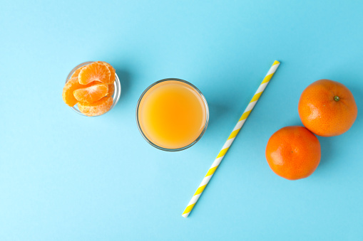 Glass of mandarin juice, straw and ingredients on blue background
