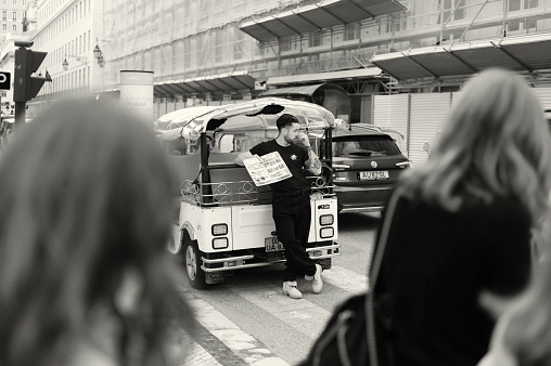 Lisbon, Portugal - Mars 11, 2023: A tuk-tuk driver waits for clients while holding a menu card in Lisbon downtown.