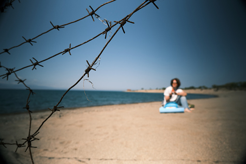 Woman is having a rest on the mountain lake. View through barbed wire