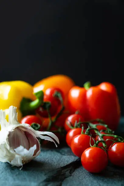 Cherry tomatoes, peppers and garlic on a slate background